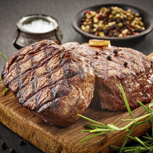 grilled beef steaks with spices on wooden cutting board