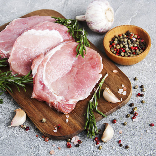 Fresh raw pork chops with spices and herbs on a stone background