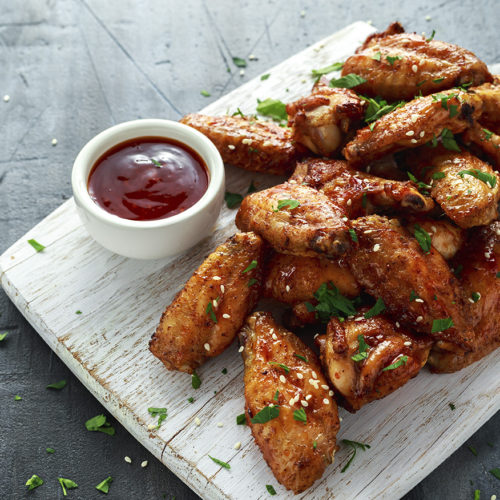 Baked chicken wings with sesame seeds and sweet chili sauce on white wooden board